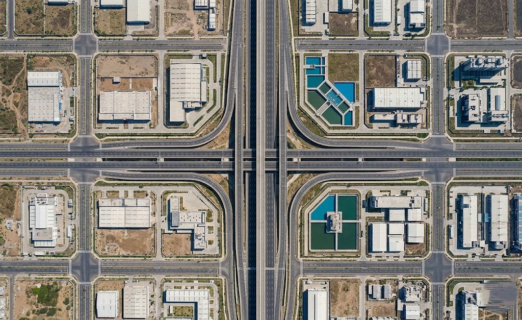 Top-down aerial view of a meticulously planned section of Dholera Smart City in India, showing modern roads, precise construction grids, water storage, and industrial buildings, demonstrating strong infrastructure development and smart urban planning.